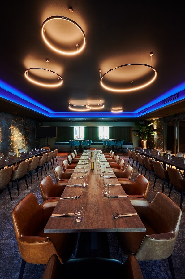 Mat zwart spanplafond in restaurant met blauwgekleurde led-strip om het plafondelement met moderne hanglampen