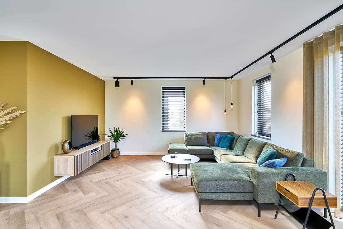 Moderne, gezellige woonkamer met visgraatvloer en mat wit Plameco spanplafond met ingebouwde verlichting rails.